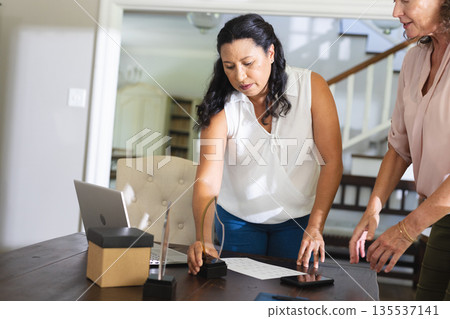 Senior women organizing documents and awards on table in home office setting Senior women organizing documents and awards on table in home office setting 135537141