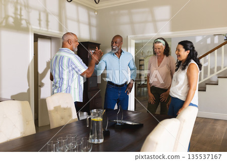 Celebrating at home, senior friends sharing laughter and high-fives around dining table Celebrating at home, senior friends sharing laughter and high-fives around dining table 135537167