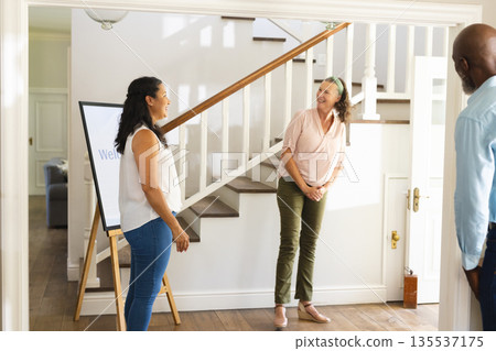 Welcoming guests at home, diverse group smiling and chatting near staircase Welcoming guests at home, diverse group smiling and chatting near staircase 135537175