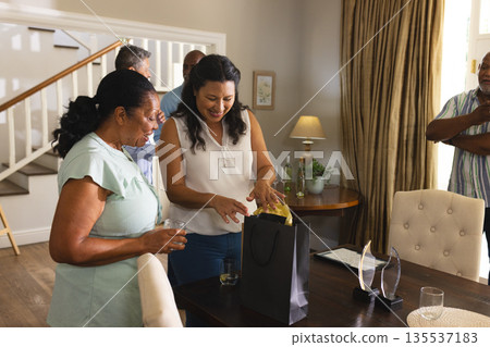 Smiling women opening gift bag at home during family celebration, enjoying moment 135537183