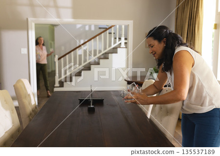 Woman setting dining table with glasses, preparing for celebration at home 135537189