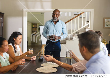 African American man leading group discussion at home, everyone holding drinks African American man leading group discussion at home, everyone holding drinks 135537238