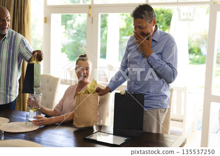 African American man opening gift bag at home, smiling with friends celebrating African American man opening gift bag at home, smiling with friends celebrating 135537250