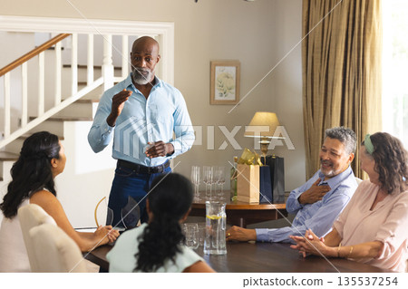 Giving speech at family gathering, African American man, everyone smiling attentively Giving speech at family gathering, African American man, everyone smiling attentively 135537254
