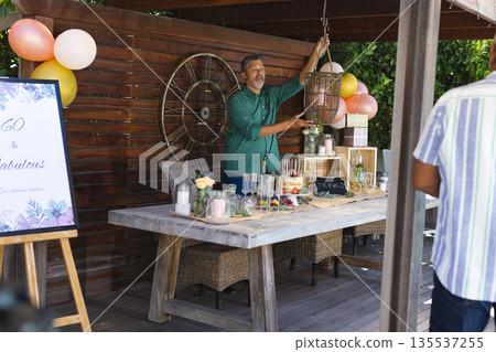 Man decorating outdoor party table with balloons and drinks for celebration 135537255