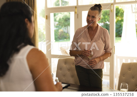 Senior woman enjoying conversation with friend while holding wine glass at home Senior woman enjoying conversation with friend while holding wine glass at home 135537258