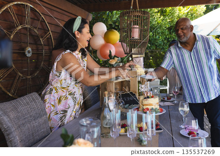 Smiling woman serving cake to African American man at outdoor birthday celebration 135537269