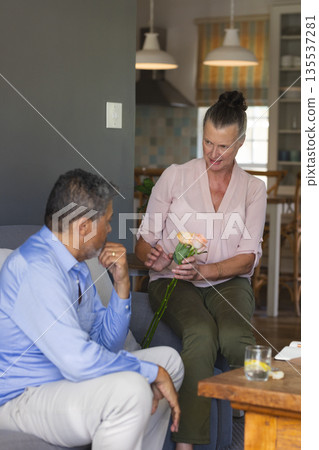 Senior woman giving flowers to man at home, both smiling and enjoying conversation 135537281