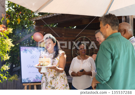 Blowing out candles, woman celebrating birthday outdoors with friends, all smiling Blowing out candles, woman celebrating birthday outdoors with friends, all smiling 135537288