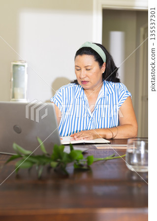 Senior woman working on laptop at home, writing notes and concentrating Senior woman working on laptop at home, writing notes and concentrating 135537301