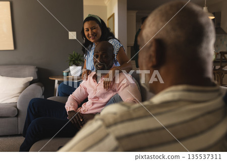 African American man sitting on sofa smiling with friends at home gathering African American man sitting on sofa smiling with friends at home gathering 135537311