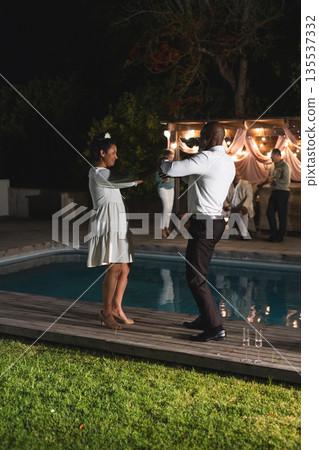 Senior couple dancing joyfully by poolside during evening celebration outdoors Senior couple dancing joyfully by poolside during evening celebration outdoors 135537332