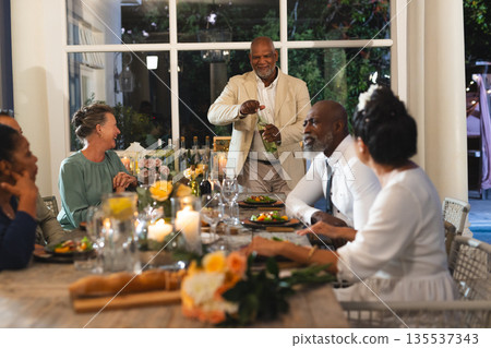 Senior man joyfully giving toast at dinner party with friends in garden setting Senior man joyfully giving toast at dinner party with friends in garden setting 135537343