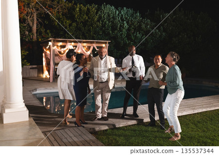 Group of diverse seniors celebrating by poolside, enjoying drinks and laughter 135537344