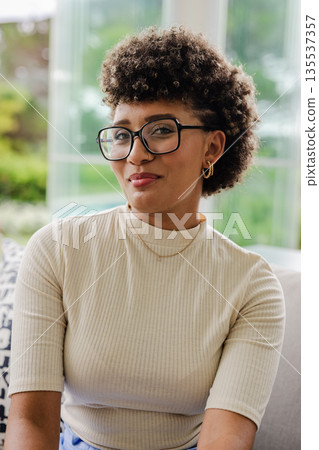 Smiling woman with glasses sitting on sofa, enjoying relaxed moment indoors 135537357