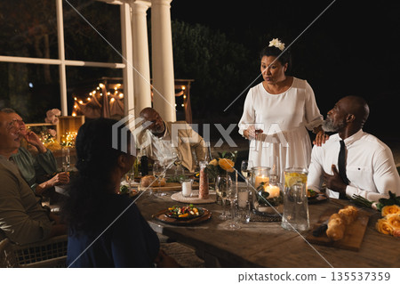 Giving speech at outdoor dinner party, African American woman engaging attentive guests Giving speech at outdoor dinner party, African American woman engaging attentive guests 135537359