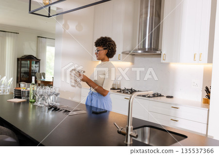 Woman in modern kitchen drying glassware, preparing for elegant dinner party Woman in modern kitchen drying glassware, preparing for elegant dinner party 135537366