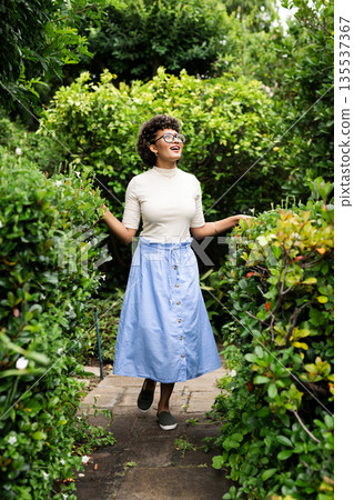 Smiling woman walking through lush garden, enjoying nature and fresh air 135537367