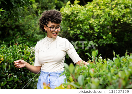 Smiling woman exploring lush garden, enjoying nature on sunny day 135537369