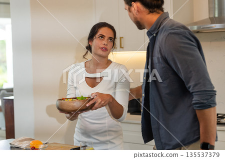 Couple in kitchen preparing salad together, sharing conversation and laughter Couple in kitchen preparing salad together, sharing conversation and laughter 135537379