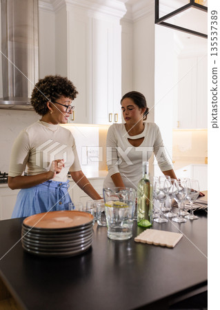 Two women in kitchen preparing drinks and chatting during wedding celebration Two women in kitchen preparing drinks and chatting during wedding celebration 135537389