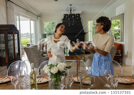 Two women joyfully preparing dining table for celebration in elegant dining room Two women joyfully preparing dining table for celebration in elegant dining room 135537391