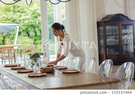 Woman arranging elegant table setting for wedding reception in bright dining room 135537404