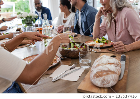 Friends enjoying meal together, sharing laughter and conversation at dinner table Friends enjoying meal together, sharing laughter and conversation at dinner table 135537410