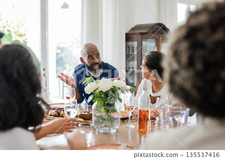 Family enjoying conversation around dining table with flowers and drinks at home Family enjoying conversation around dining table with flowers and drinks at home 135537416