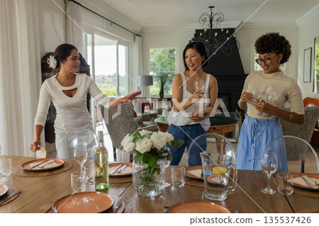 Women joyfully setting dining table with wine glasses and plates at home Women joyfully setting dining table with wine glasses and plates at home 135537426