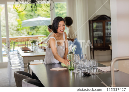 Woman arranging glassware on table, preparing for elegant indoor wedding reception Woman arranging glassware on table, preparing for elegant indoor wedding reception 135537427