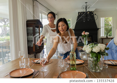 Setting elegant table with wine glasses and plates, women preparing for celebration Setting elegant table with wine glasses and plates, women preparing for celebration 135537428
