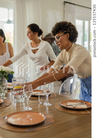 Setting elegant dining table, women arranging flowers and glassware for wedding celebration 135537430