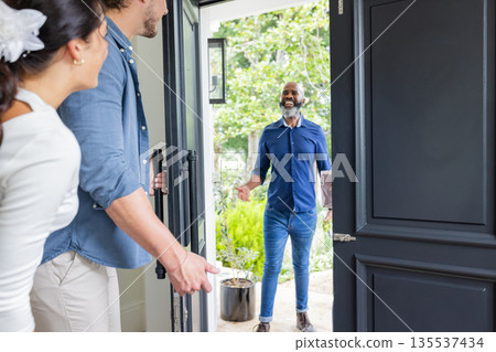 Welcoming guest at home, smiling couple greeting friend at front door Welcoming guest at home, smiling couple greeting friend at front door 135537434
