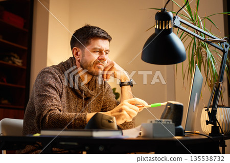 Man working at desk with laptop in home office Man working at desk with laptop in home office 135538732