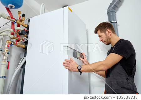 Technician installing heat pump system with pipes and expansion tank 135538735