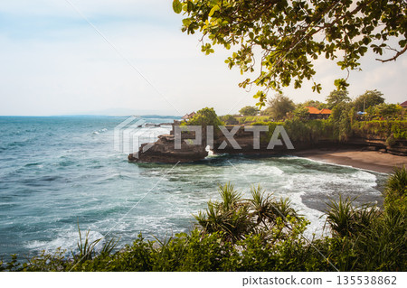 Scenic coastal landscape near Tanah Lot, dramatic ocean waves crashing on rugged cliffs. Tropical foliage and lush green vegetation, perfect for Bali travel, nature escape stock photography Scenic coastal landscape near Tanah Lot, dramatic ocean waves crashing on rugged cliffs. Tropical foliage and lush green vegetation, perfect for Bali travel, nature escape stock photography 135538862