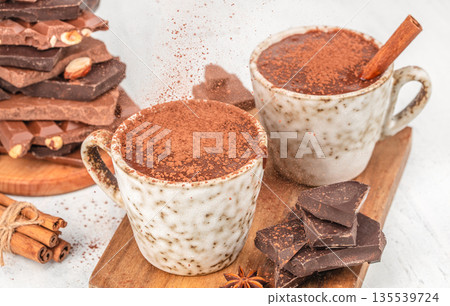 Two cups of hot chocolate with cocoa powder and chocolate pieces on white background 135539724
