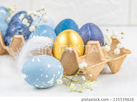 Elegant Easter eggs in cardboard carton with blue and gold colors, spring flowers and soft light Elegant Easter eggs in cardboard carton with blue and gold colors, spring flowers and soft light 135539828