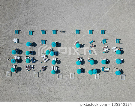 Sea relax under beach umbrella. Travel to sea. Aerial top view of sand exotic beach with sunbed and umbrella. People on beach enjoying sun. Summer vacation. Beach vacation at sea in summer 135540154