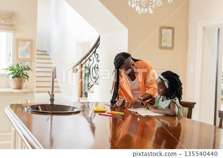 Helping with homework, mother and daughter at kitchen table, focusing on learning Helping with homework, mother and daughter at kitchen table, focusing on learning 135540440