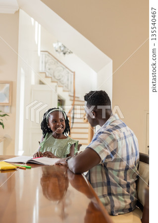 African American father helping daughter with homework at home, both smiling warmly 135540467