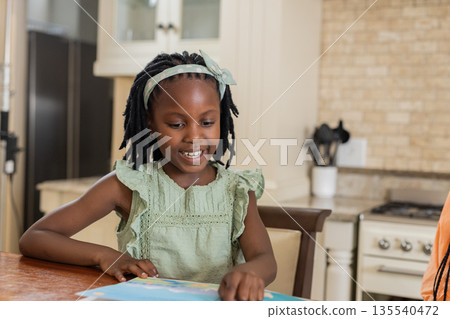African American girl reading book at home, smiling and enjoying her time African American girl reading book at home, smiling and enjoying her time 135540472