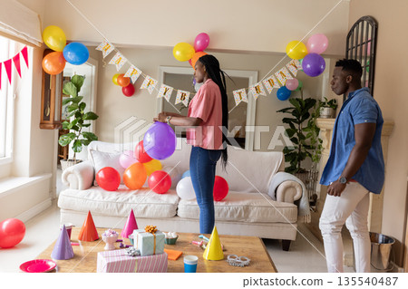 Decorating living room with balloons, African American couple preparing birthday celebration 135540487