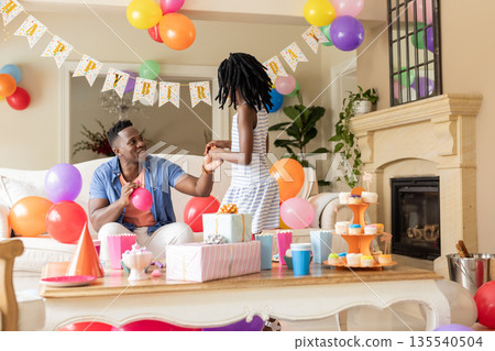 Father and daughter celebrating birthday at home with balloons and gifts Father and daughter celebrating birthday at home with balloons and gifts 135540504