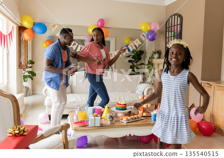 African American family celebrating birthday at home with cake and colorful balloons African American family celebrating birthday at home with cake and colorful balloons 135540515