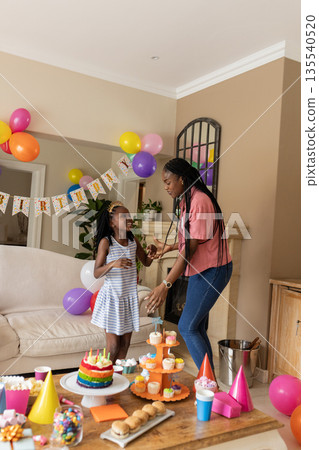 Mother and daughter celebrating birthday at home with colorful decorations and cake Mother and daughter celebrating birthday at home with colorful decorations and cake 135540520
