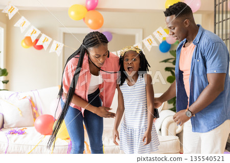 Family celebrating birthday at home, decorating with balloons and colorful banners Family celebrating birthday at home, decorating with balloons and colorful banners 135540521