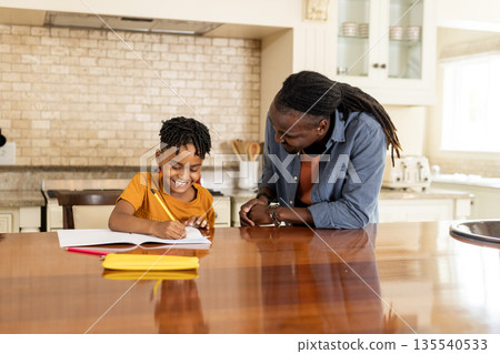 African American father helping son with homework at kitchen table, both smiling African American father helping son with homework at kitchen table, both smiling 135540533