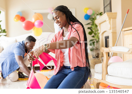 Decorating living room with balloons, African American couple smiling for celebration 135540547